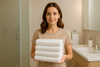 An image of a woman holding up bath towels wondering how many bath towels do i need