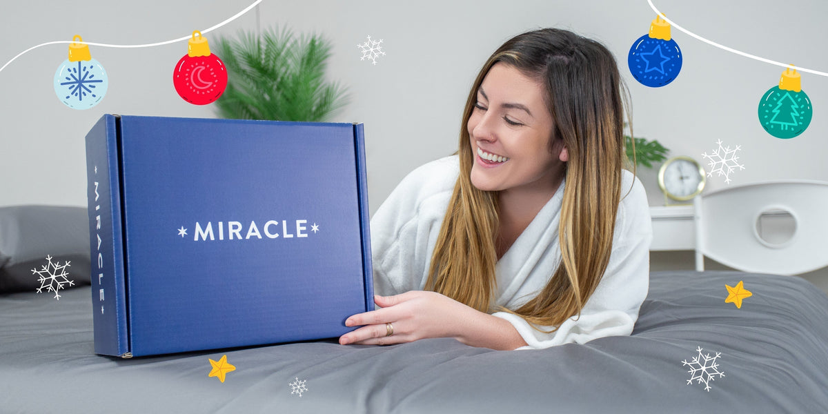 Woman laying on a bed smiling at a Miracle Brand box.
