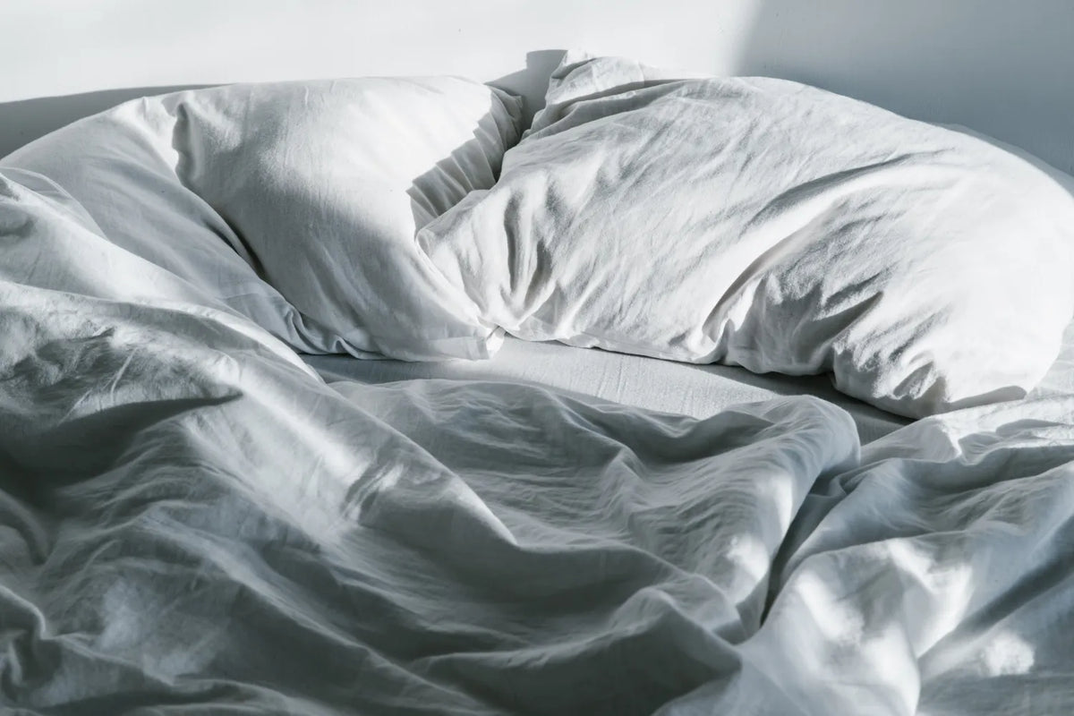 Unmade bed with wrinkled white sheets and pillows