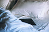 A tablet sitting on a bed next to a white pillow.
