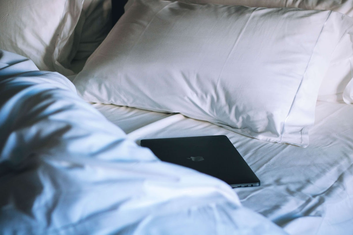 A tablet sitting on a bed next to a white pillow.