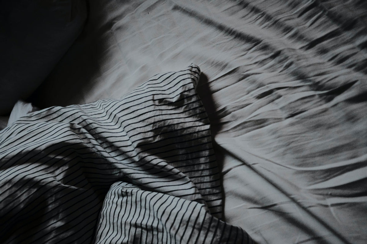 Striped pillow laying on a bed with grey sheets.