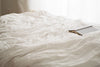 A book laying open on a king size bed with white sheets.