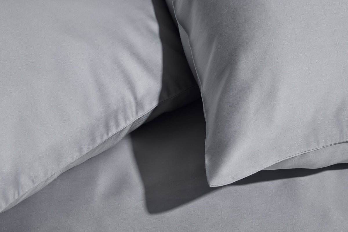 Close-up of two smooth, grey pillowcases resting on a matching grey sheet, highlighting the soft fabric texture and clean seams.