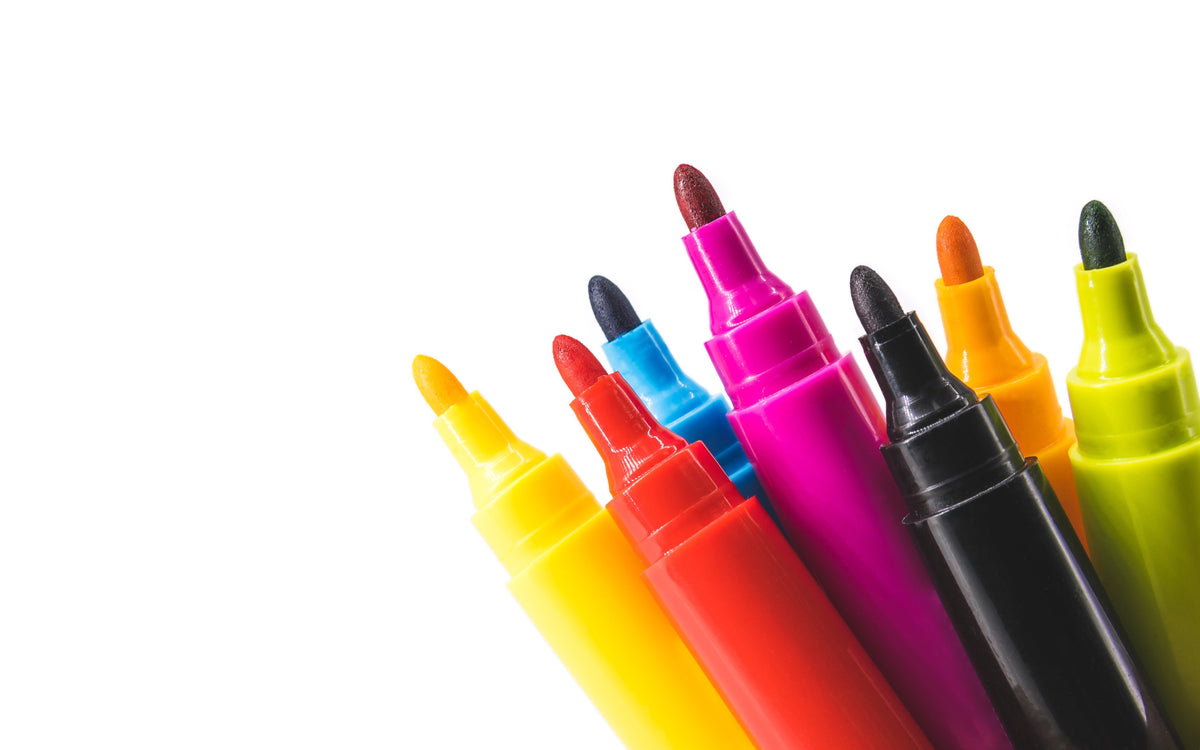 A group of uncapped, vibrant felt-tip markers in yellow, red, blue, pink, black, orange, and lime green, arranged diagonally against a white background.