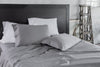 A styled bed with a black headboard featuring smooth grey sheets and a mix of grey and white pillowcases, creating a clean and modern aesthetic.
