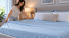 A woman putting a new cooling sheet on the bed.