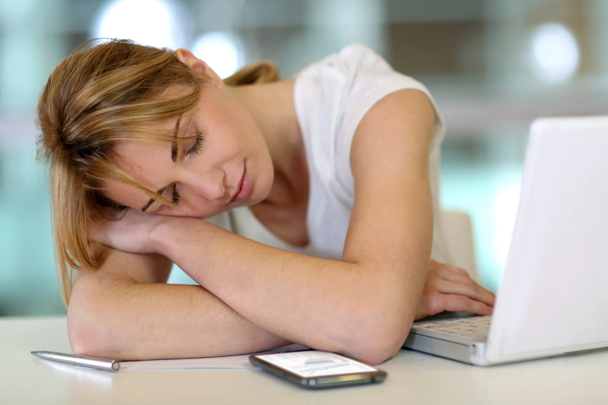 Tired woman resting head on arms while working on laptop