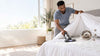 A black man vacuuming the bed for dust mites.