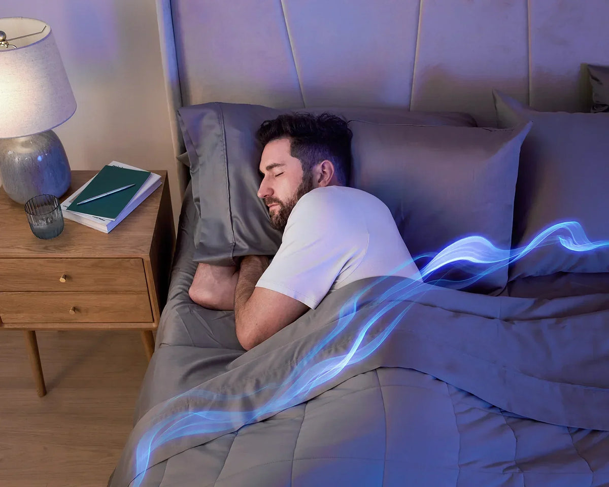 A man sleeping comfortably on his side under a Stone grey Miracle Made cooling comforter, with a blue light graphic overlay illustrating temperature regulation and airflow.