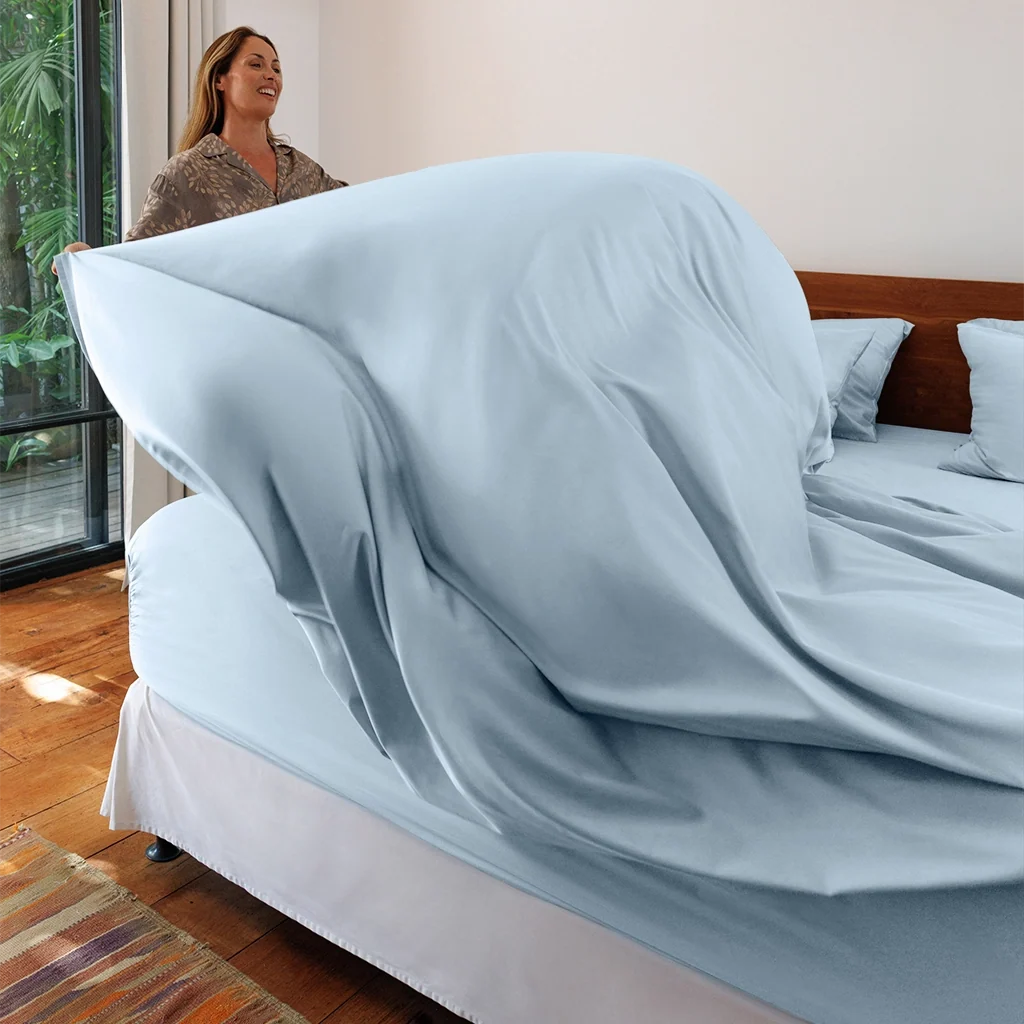 A woman putting a sheet on the bed.