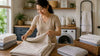 An asian woman folding a bed sheet.