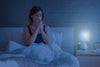 Woman sick in bed at night with tissues and bedside lamp