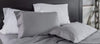 A close-up of a bed styled with a mix of light grey and white pillowcases and matching grey sheets against a dark headboard.