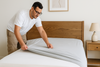 An image of a man putting bed sheets on a bed