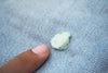 A close-up shot of a finger pointing to a piece of light green chewing gum stuck to blue denim fabric.