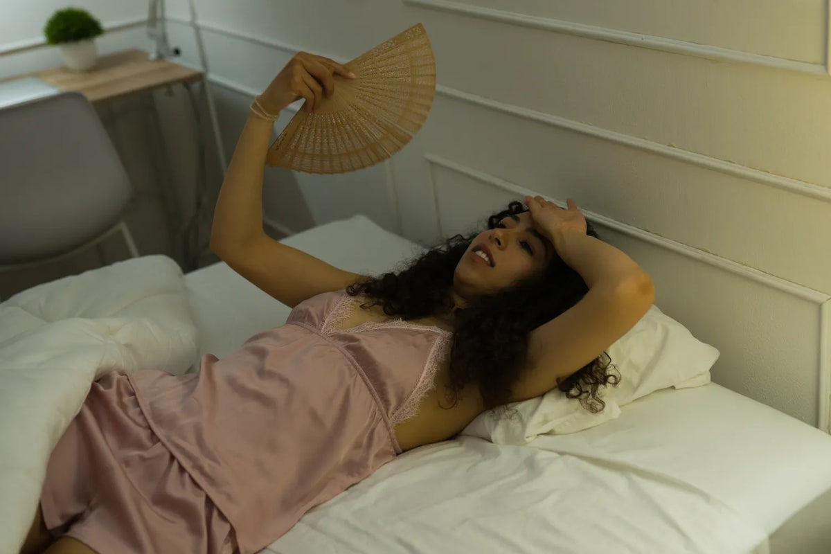 Woman feeling overheated in bed while trying to cool down at night