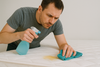 A man using a spray bottle and a piece of cloth to clean the mattress