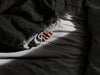 A dramatic high-contrast shot of a hand clutching the edge of a dark grey duvet on a bed with light-colored wrinkled sheets, illuminated by a sliver of morning sunlight.