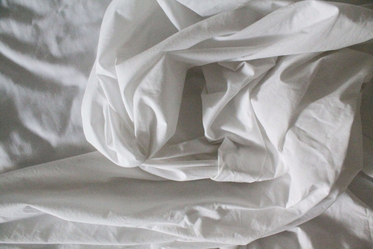 Wrinkled deep pocket sheets sitting on a white bed.