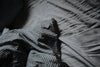 Striped pillow laying on a bed with grey sheets.