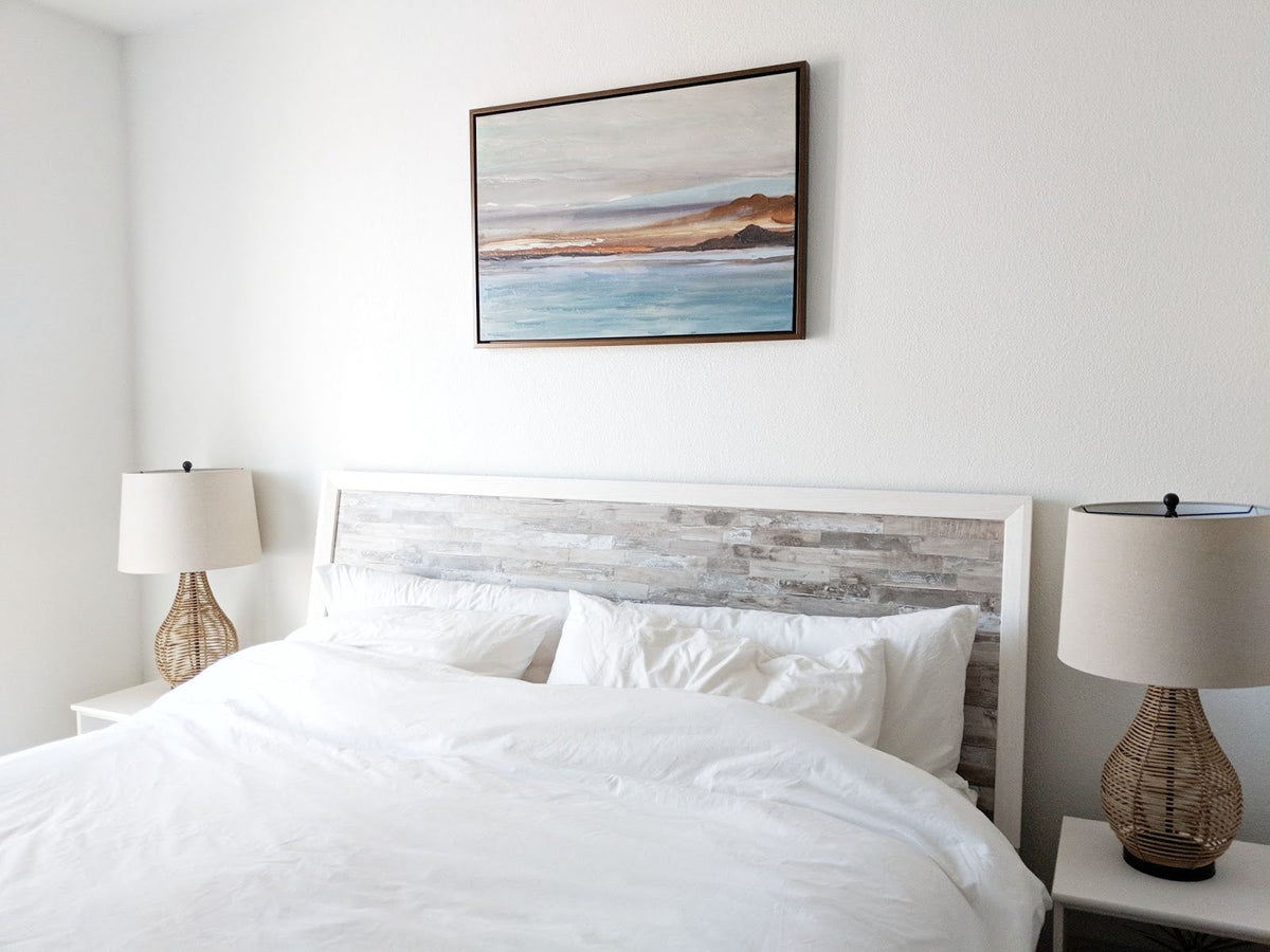 A large white bed with a picture of a beach hanging above it.