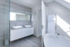 A sleek, all-white modern bathroom featuring a double vanity with vessel sinks, a floating white cabinet, and a freestanding oval bathtub with a grey bath caddy.