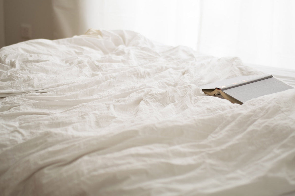 A book laying open on a king size bed with white sheets.