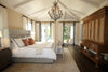 Elegant bedroom with a large bed, white bedding, chandelier, wooden furniture, and tall windows letting in natural light.