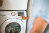 Person pressing the control panel buttons on a front-loading washing machine.