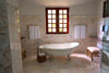 A luxury marble-tiled bathroom featuring a white clawfoot bathtub, white towels on wall-mounted racks, and a large wooden window that lets in natural light.