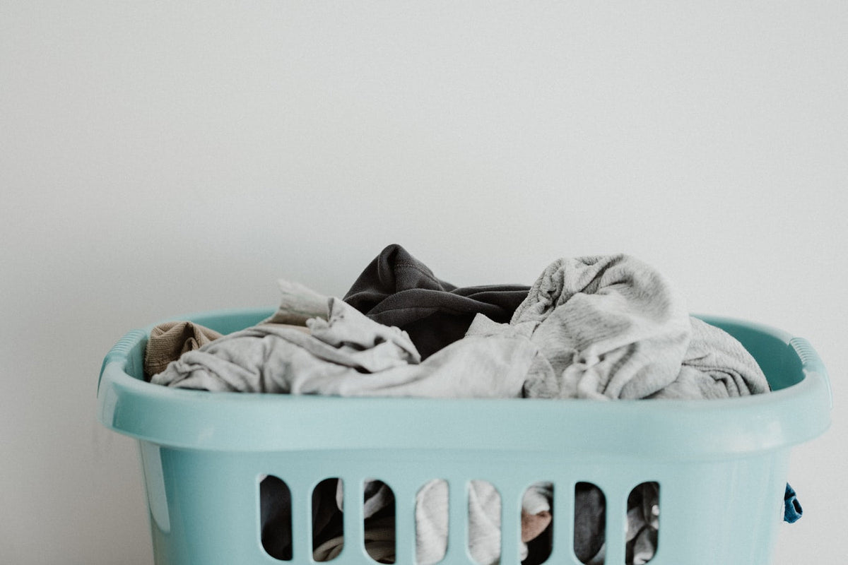 Laundry basket filled with mixed clothes against a light background.