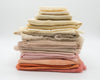 A stack of neatly folded fabrics in a warm gradient of colors, ranging from off-white and cream at the top to soft pink, peach, and terracotta at the bottom.