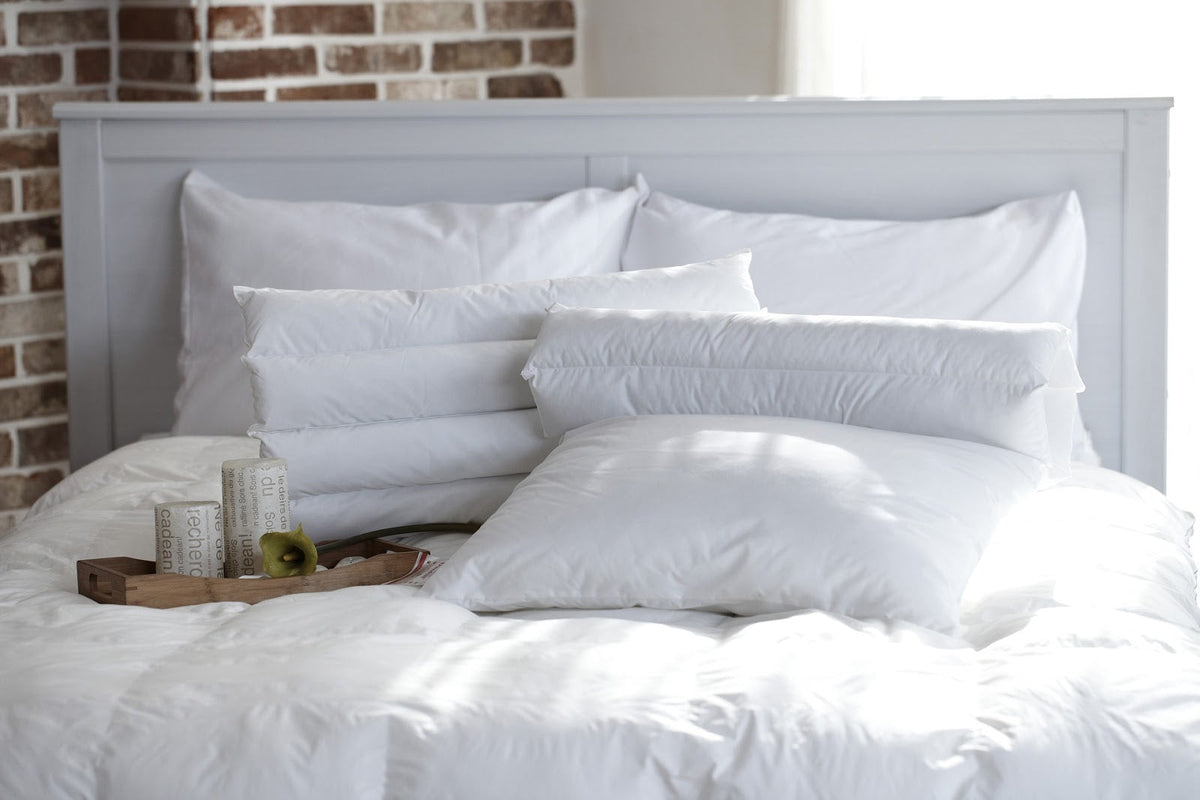 A tea pot and pillows sitting on a white bed.