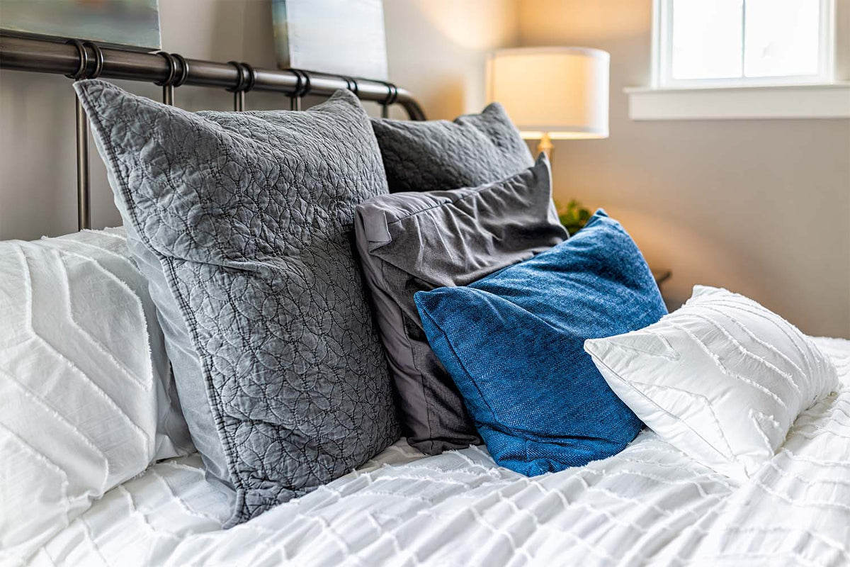 Bed with white bedding layered with gray and blue decorative pillows.