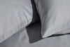Close-up of two smooth, grey pillowcases resting on a matching grey sheet, highlighting the soft fabric texture and clean seams.