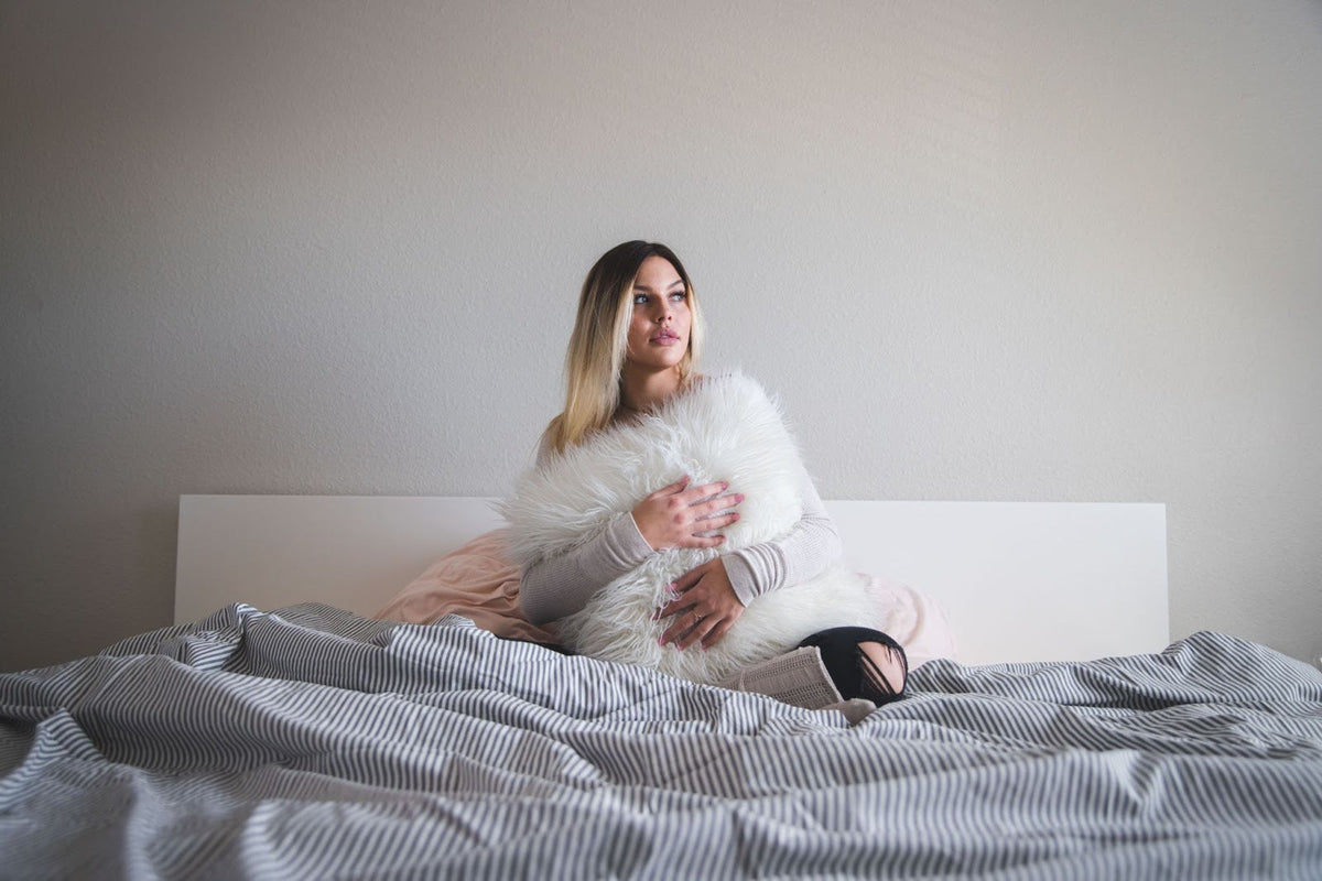 Woman sitting on a bed holding a fluffy white pillow.
