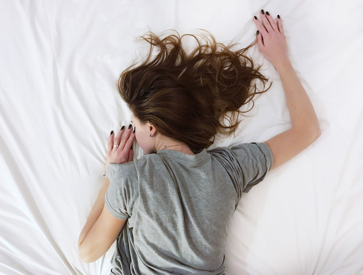 Woman laying face down on a bed with white sheets.