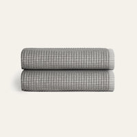 Two folded gray textured blankets stacked on a light beige background