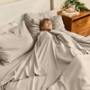 Woman lying in bed under gray bedding with a wooden nightstand in the background