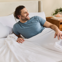 Man lying in bed wearing a blue shirt, smiling.