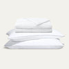 Stack of white pillows and a folded white blanket on a light gray background