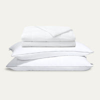 Stack of white pillows and a folded white blanket on a light gray background