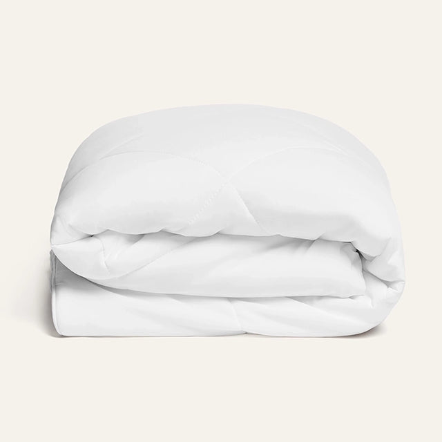 Folded white comforter on a light beige background