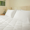 White quilted comforter on a bed with pillows in a bedroom setting.