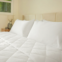 White quilted comforter on a bed with pillows in a bedroom setting.
