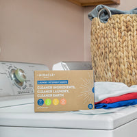 Box of Miracle Make laundry detergent sheets on a washing machine with clothes and a basket in the background.