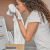 Woman holding a white towel next to a box of Miracle Care laundry detergent sheets.