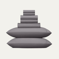 Stack of gray pillows and bed sheets on a white background
