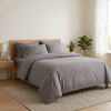 Bedroom with a bed covered in gray bedding and pillows, wooden headboard, and plants.